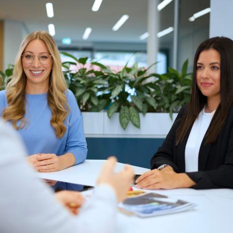 zwei junge Mitarbeitende stehen am Tisch und unterhalten sich.