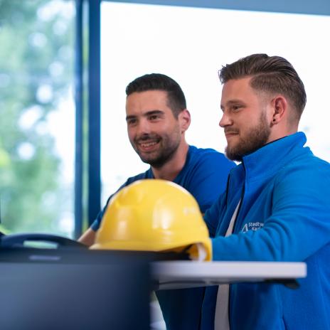 zwei gewerblich-technische Mitarbeitende stehen am Schreibtisch