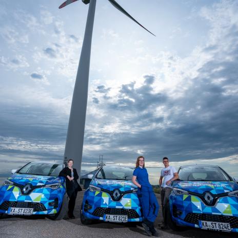 Bild mit drei Studierenden vor Elektroautos