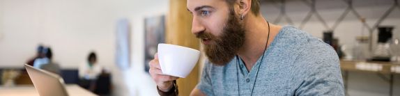 Mann mit Kaffeetasse in der Hand sitzt vor einem Computer
