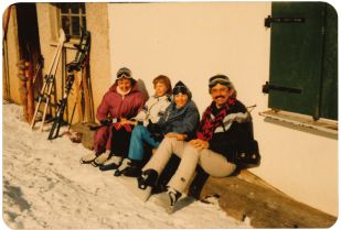 Familie im Skiurlaub sitzend auf einer Bank vor einem Haus