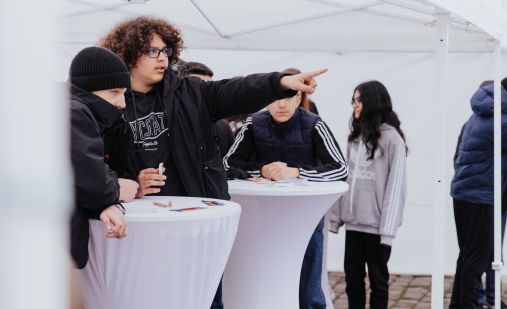 Schulklasse steht um weiße Tische herum